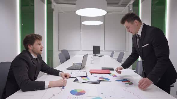 Side View of Angry Successful Businessman Throwing Paperwork Over Table to Manager Talking and alt