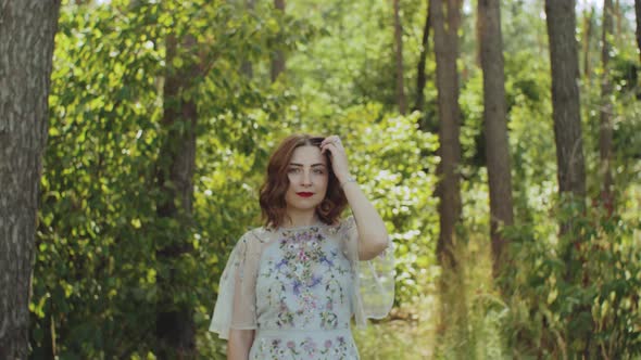 Attractive Woman with Red Lips Touches Her Curly Hair Walk in the Forest Slow Motion alt
