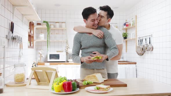 Asia gay couple using tablet and preparing the breakfast, sandwich vegetable on table in kitchen.