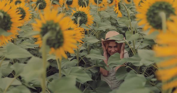 Beautiful Young Woman Walks Through Huge Sunflowers and Straightens the Hat with Her Hands