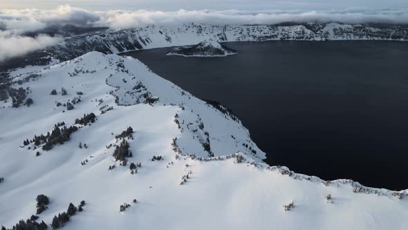 Drone shot of snowy shores of volcanic caldera lake, Crater Lake, Oregon, USA alt
