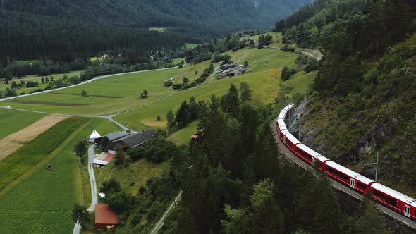 Drone Tracking Famous Red Glacier Express Train Cruising Through Majestic Summer Switzerland Alps alt