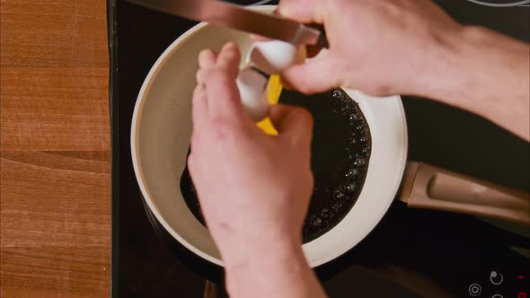 Male Hands Break an Egg Into a Frying Pan in Black Oil
