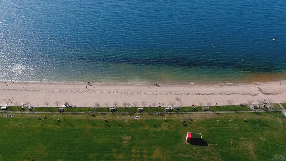 Lake beach with people sunbathing and bathing, garden and walking area. Overhead drone shooting trav alt