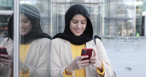Smiling woman wearing hijab and using smartphone