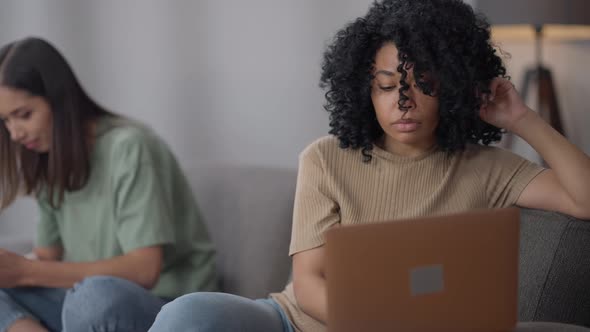 Thoughtful Focused African American Slim Young Woman Surfing Internet on Laptop in Home Office with alt