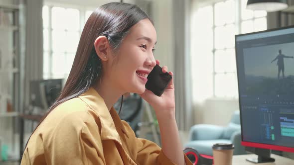 Asian Female Video Editor Works And Talking On Mobile Phone With Her Personal Computer In Office alt