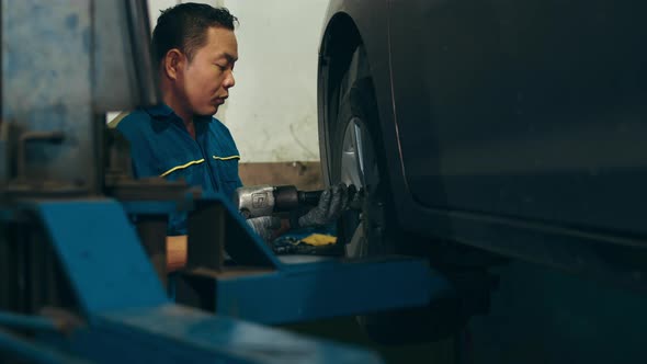 Skillful Asian guy in uniform fixing car at mechanics garage at night. alt