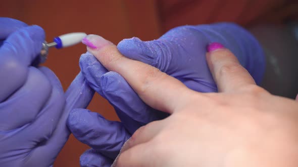 Manicure master in blue gloves removes gel polish from nails using a cutter. alt