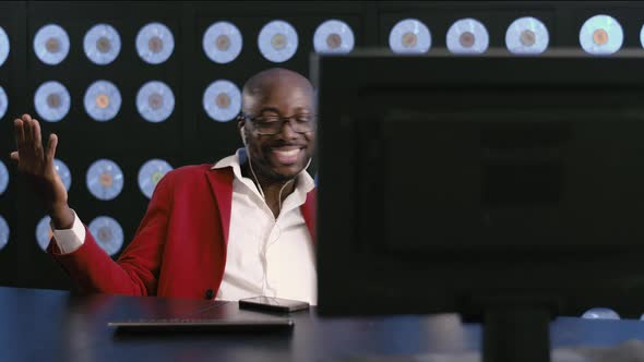 Attractive Black Man in Red Suit Sits at Desk Listens to Music and Dances