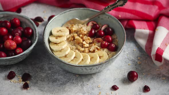 Ceramic Bowl of Oatmeal Porridge with Banana, Fresh Cranberries and Walnuts alt