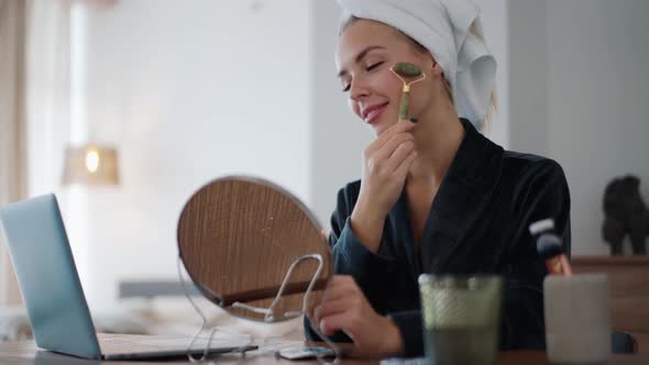 Positive woman with a towel on her head doing massage with a guasha roller alt