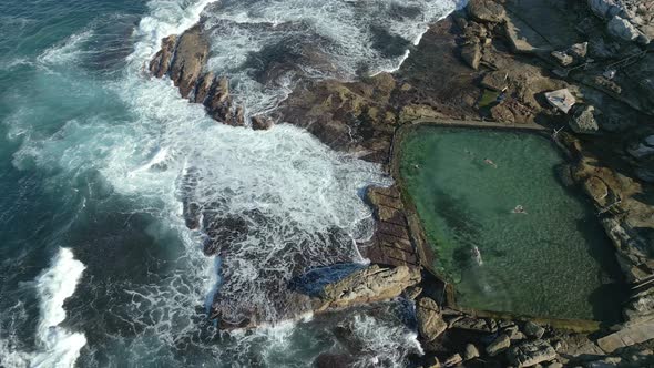 Ocean waves crashing on the rocks. People swimming in a rockpool by the rocky beach at Maroubra, Syd alt