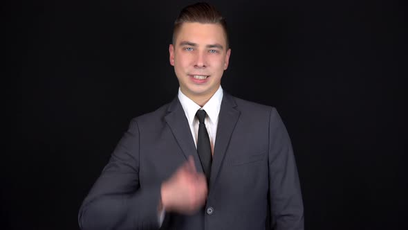 Young Businessman Shows Like on Hand. Man in a Black Suit on a Black Background alt