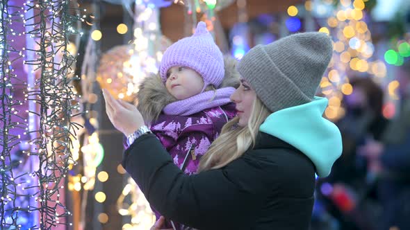 Happy mom and her little daughter choose holiday decorations at the street Christmas market alt