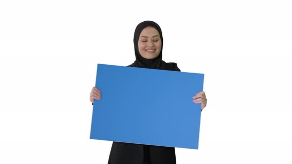 Smiling Arab Woman in Hijab Holding Blank Blue Poster and Looking at It on White Background. alt