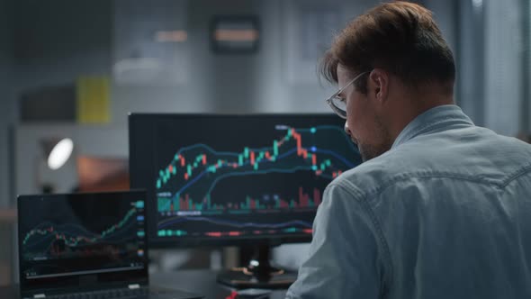 Rear View of Trader Working with Stock Market on Laptop Late in Office alt
