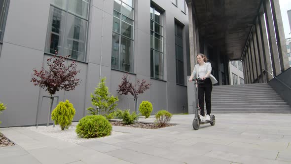 Young Successful Woman Rides an Electric Scooter on a Sunny Day and Enjoys Life on a Background of alt
