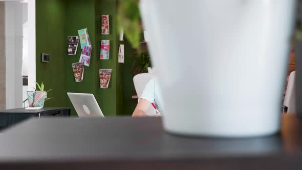 Creative Young Designer Writing Notes and Working on His Laptop at the Office alt