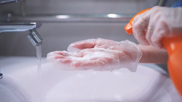 Woman in Gloves Washes the Faucet and Sink in the Bathroom, Sprays Foam on a Rag, Daily Cleaning and alt