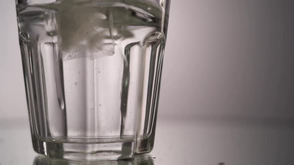 Close Up Ice Falls in a Glass of Water Slow Motion. Morning Light on the Floor Where a Transparent alt