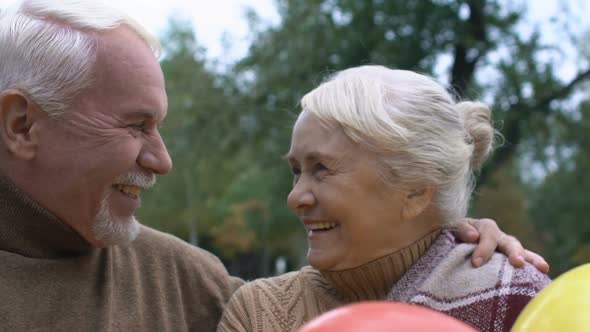 Cheerful Mature Couple Smiling Holding Air Balloons, Anniversary Celebration