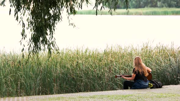 Woman Playing a Guitar By the Banks of the River. alt
