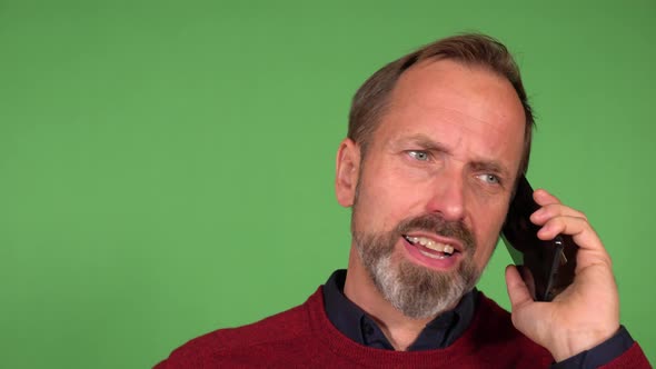 A Middleaged Caucasian Man Talks on a Smartphone and Picks His Nose  Closeup  Green Screen