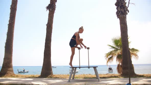 Gymnastics By the Sea  a Young Blonde Woman Stands Up on the Small High Beam alt