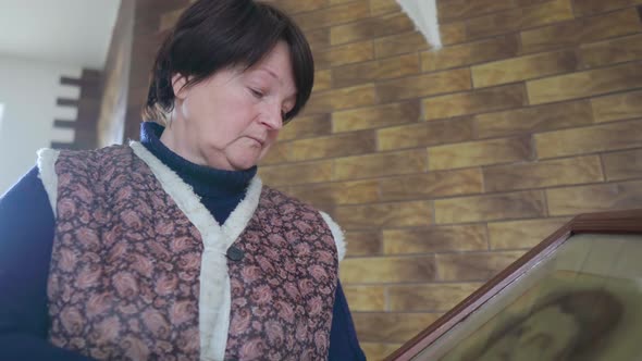 Elderly Woman Becoming Sad While Holding and Looking at Old Photo Portrait of Ancestor