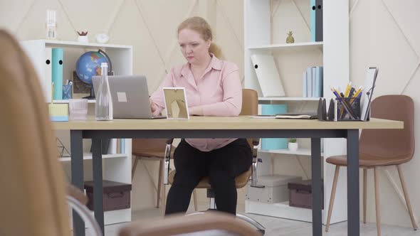 Wide Shot of Serious Woman Working with Laptop in Office and Rubbing Neck. Portrait of Concentrated alt