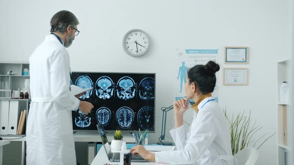 Doctors Male and Female Analyzing Brain Scans and Discussing Disease in Hospital Room alt