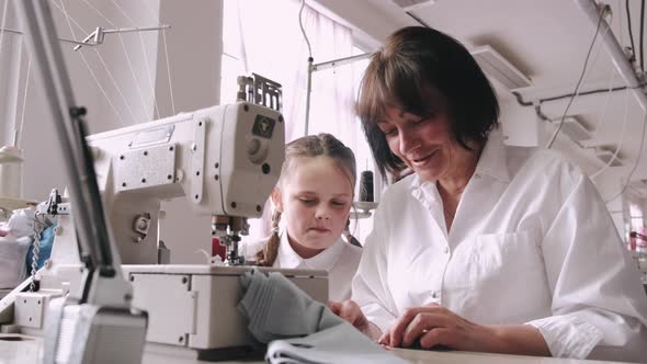 Grandma with Little Granddaughter Sew Clothes in the Factory alt