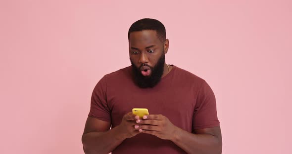 Young African American Man Using Phone Surprised Isolated on Pink Background alt