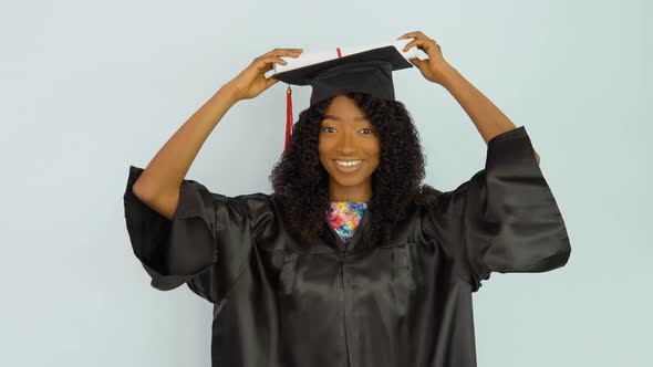 A Young African American Woman in a Black Gown and a Master's Hat Stands Upright Holding a Diploma alt