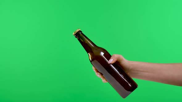 A Female Hand Passes a Dark Brown Bottle with Beer or Lemonade to a Male Hand Isolated on a Green alt
