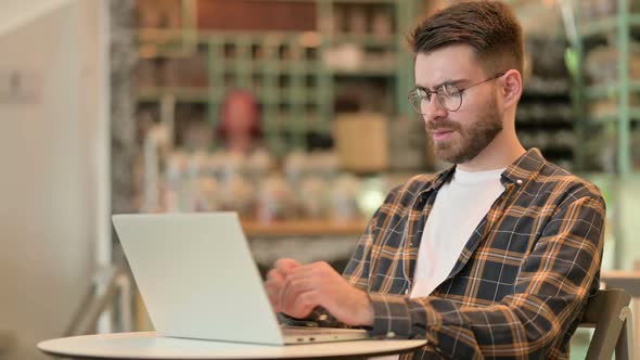 Young Male Deisgner with Laptop Haing Wrist Pain in Cafe alt