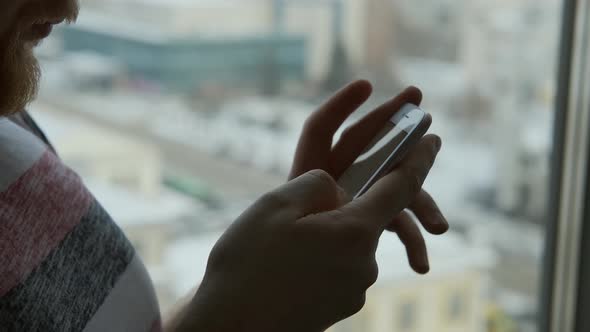 close-up of a bearded man using a smartphone by the window