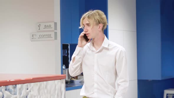 Portrait of Serious Millennial Blond Man Talking on the Phone Standing in Office Corridor alt