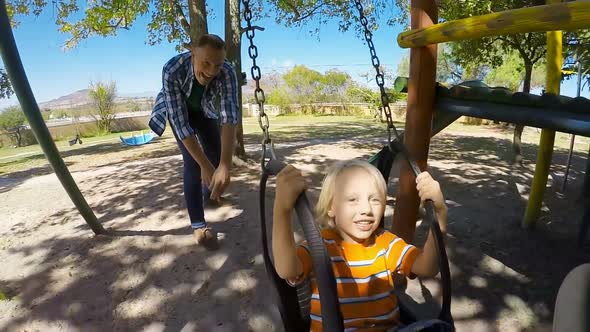 Father pushing son on swing in the park 4k alt