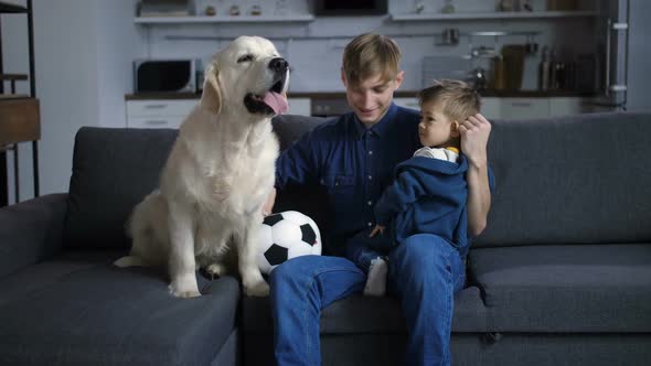 Father with Toddler Son and Dog Sitting on Sofa alt