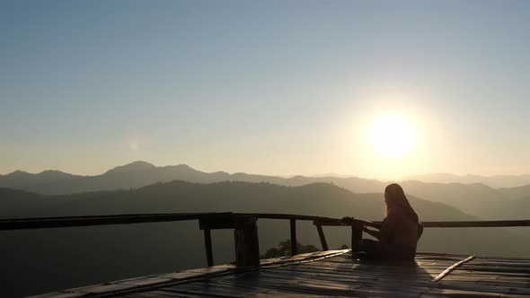 Rear view of a female sitting and playing guitar on wooden balcony