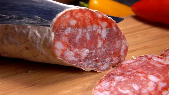 Dry Sausage in White Skin Is Cut with a Knife alt