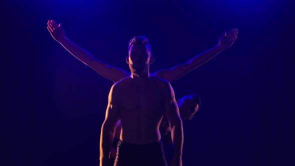Group of Acrobatic Gymnasts Perform Acrobatic Exercises. Shot in a Dark Studio with Blue Light. Slow alt