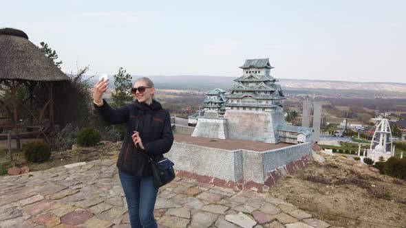 Girl Takes a Selfie Near a Miniature Chinese Japanese Pagoda. Park of Miniatures. alt