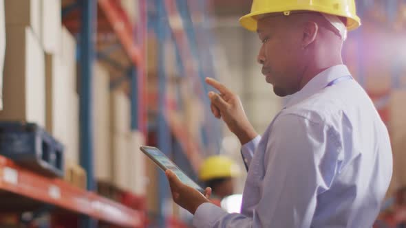 African american male worker with helmet using smartphone in warehouse alt