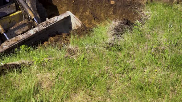 Excavator Bucket Removing Layer of Soil with Grass During Earth Works alt