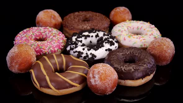Different donuts with icing and colorful sprinkle rotating on a black background. 