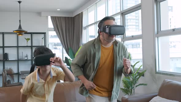 Asian father and son playing a game fighter using VR Headsets with mother cheering.
