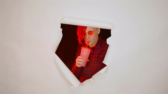 Young Man in Red Plaid Shirt Drinking Through Soft Drink Straw in Hole of White Background alt